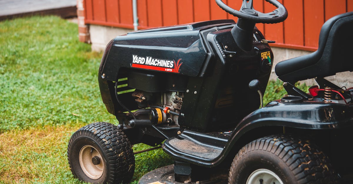Close-up of a black riding lawn mower parked on a lawn next to a red building.